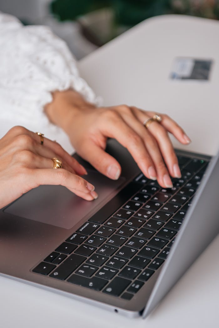 Home Hands of a woman typing on a laptop keyboard indoors, showcasing rings and fashion.